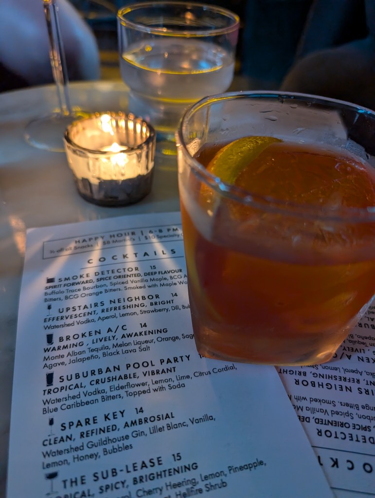 A cocktail on a table arranged with candle, menu, and water glass